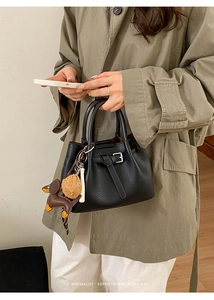 Detail der schwarzen Handtasche aus genarbtem Leder mit Schnalle und niedlichen Anhängern