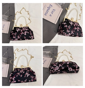 Close-up of pink cherry blossom embroidery on a black satin evening bag with pearl handle