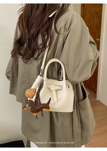 Detail der cremeweißen Lederbeuteltasche mit Gürtelschnalle und Hundeanhänger am Model