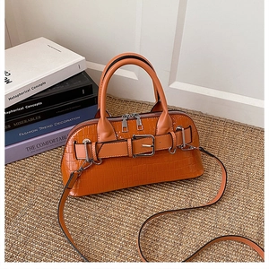 Close-up of orange crocodile pattern shell handbag on woven mat with fashion books