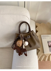 Detail der braunen Lederhandtasche mit Gürtelschnalle und süßem Hunde-Anhänger