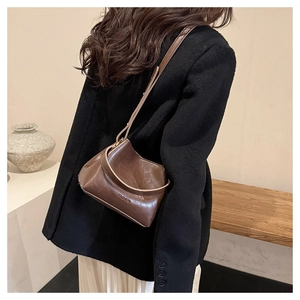 Close-up of a brown leather bucket bag featuring elegant metal Fashion lettering and strap