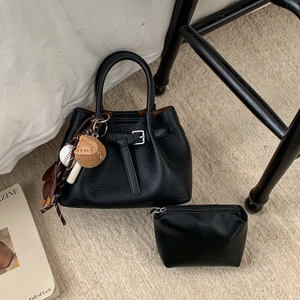 Detail einer schwarzen Lederhandtasche mit Beutel und sportlichen Anhängern im Fokus
