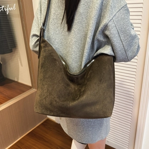 Brown suede crossbody dumpling bag with wide strap worn by a model in casual home setting
