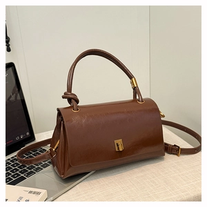 Brown faux leather handbag with a gold twist-lock closure on a white textured background