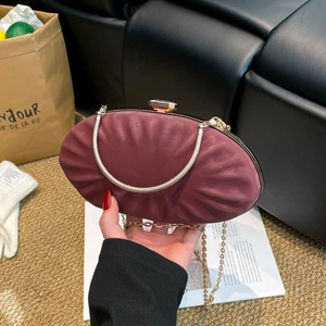 Pochette ovale bordeaux avec fermoir pierre précieuse et chaîne dorée en main