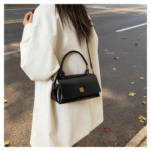 Detail of a black glossy leather handbag with gold buckle and knotted handle on a model