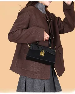 Detail of black trapezoid leather handbag with golden lock worn with brown wool coat