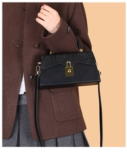 Detail of black rectangular crossbody bag with gold lock buckle and top handle over coat