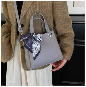Detail of grey pebbled leather handbag with silk scarf handle on model in tweed jacket