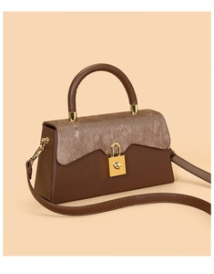 Detail of a brown leather handbag featuring a pleated metallic lid and gold clasp