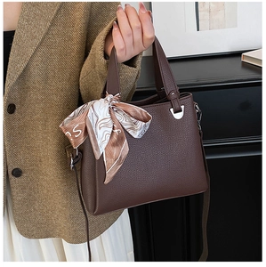Detail of coffee litchi grain leather tote bag with decorative silk scarf on handle
