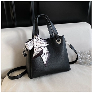 Close-up of black trapezoid leather handbag with decorative printed silk scarf on handle