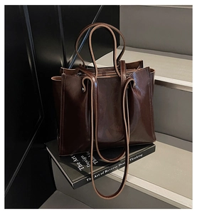 Detail of dark brown glossy leather tote bag with dual strap system on a prop book