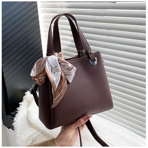 Detail of dark brown lychee leather handbag with decorative silk scarf and metal hardware