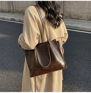 Detail of dark brown tote bag with oily leather texture worn over a khaki trench coat