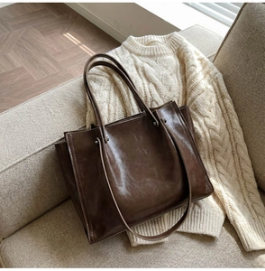 Detail of a structured dark brown leather tote bag on a white sweater in a home setting