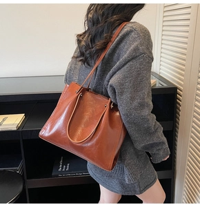 Detail of a large brown oil-wax leather tote bag with rivets shown on a model