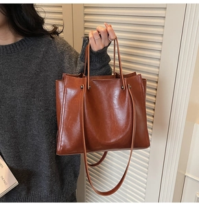 Detail of high-gloss caramel brown leather tote bag with reinforced metal rivets and stitching