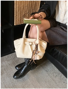 Detail of cream lychee leather handbag with metal buckle and coffee-themed charm accessory