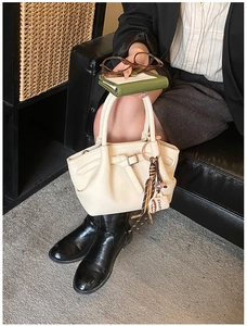 Detail of beige lychee texture handbag with metal buckle and coffee cup tassel charm