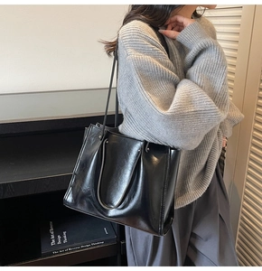 Side view of black glossy leather tote bag with shoulder straps and retro oil wax texture