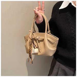 Detail of beige lychee pattern handbag with coffee charm and elegant side pleats