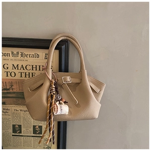 Detail of beige textured leather handbag with coffee cup charm and elegant strap buckle