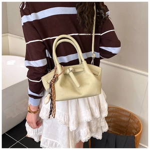 Detailed view of cream leather crossbody bag with braided tassel and pebble texture