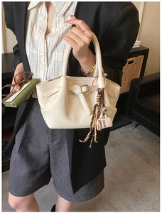Close-up of cream lychee leather handbag with a mini coffee bag charm and metal buckle