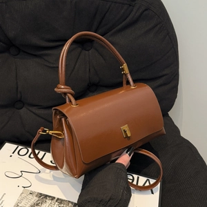 Vintage brown leather crossbody bag with knot handle and golden metal clasp on black background