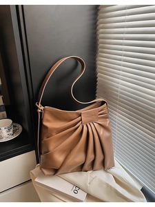 Detail of caramel pleated underarm bag with accordion folds and embossed logo tag