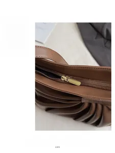 Close-up of smooth gold metal zipper and brown pleated PU leather on a shoulder bag