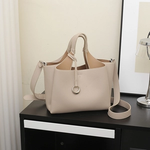 Beige faux leather tote bag with round metal charm and removable strap shown in a modern home