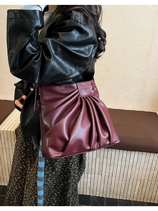 Detail of burgundy pleated leather shoulder bag worn by model with textured surface
