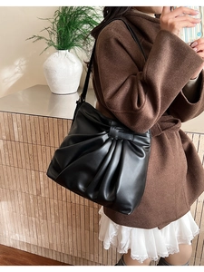 Detail of black pleated leather hobo bag with embossed logo tag in a warm lifestyle setting