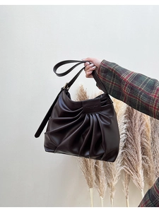 Detail of vintage pleated dark brown shoulder bag with a square logo patch and PU texture