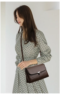 Detail of a brown leather shoulder bag featuring lychee texture and silver metal buckle