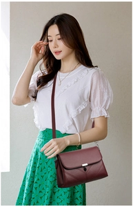 Detail of burgundy pebbled leather crossbody bag with V-shaped stitching and metal clasp