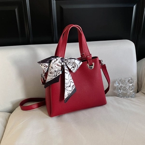 Deep red leather tote bag with decorative scarf and shoulder strap on white sofa