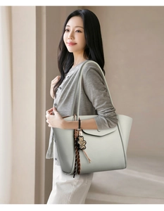 Detail of light gray leather tote bag with leopard bear charm and tassel decoration