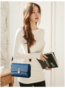 Detail of navy blue shoulder bag with golden oval twist lock and brown strap worn by model