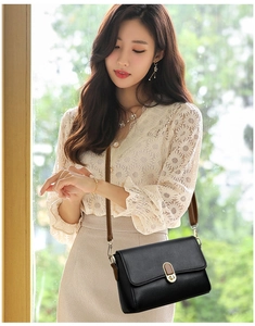 Close-up of elegant black leather handbag featuring a unique gold twist lock and brown strap