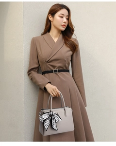 Close-up of grey leather handbag with polka dot ribbon and brown long-sleeved dress