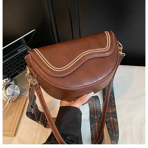 Détail du sac besace marron avec bordure ondulée, bijoux dorés et bandoulière tissée