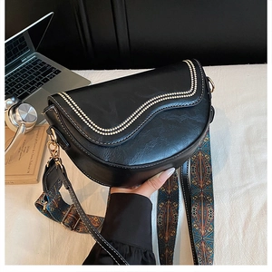 Détail du sac selle noir avec bords brodés et large bandoulière au motif ethnique