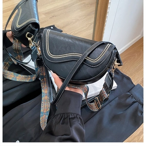 Détail du sac selle noir avec surpiqûres dorées et bandoulière en jacquard coloré