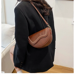Sacoche marron foncé à perles portée à l'épaule par un mannequin en veste noire