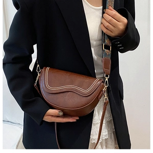 Détail du sac selle marron avec surpiqûres contrastées et bandoulière ethnique