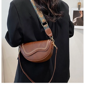 Détail du sac selle marron avec rivets ondulés et deux bandoulières amovibles sur modèle